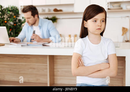 Triste perché di papà. Piuttosto piccola figlia in piedi la cucina con le braccia incrociate, guardando sconvolto perché di suo padre seduto in backgroun Foto Stock