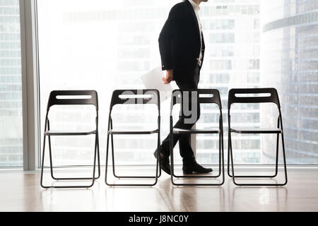 Uomo in business suit passeggiate passato sedie in fila Foto Stock