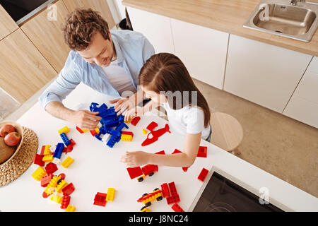 In pieno svolgimento. Upbeat sorridente padre e sua figlia piccola essendo totalmente impegnato nel giocare insieme, assemblaggio di set di costruzione e la raccolta di un pi Foto Stock