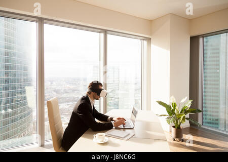 Uomo al lavoro su laptop con occhiali per realtà virtuale Foto Stock
