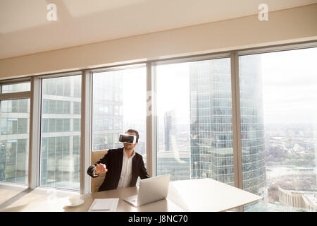 Uomo alla scrivania in VR cuffia rivolta all'aria Foto Stock