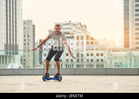 Guy riding hoverboard, sullo sfondo della città. Foto Stock