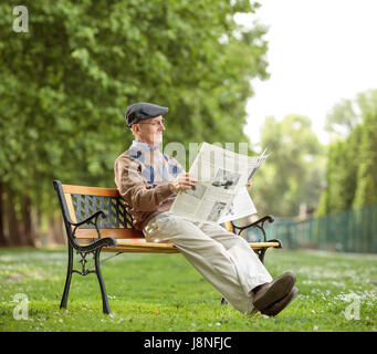 Senior seduta su una panchina e leggendo un giornale nel parco Foto Stock