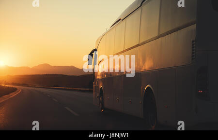 Bus bianco in marcia su una strada verso il sole di setting Foto Stock