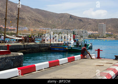 Un unico maschio da pesca alla fine del calcestruzzo jeyy nell affollata marina a Los Cristianos sull isola di Teneriffe nelle Canarie Foto Stock