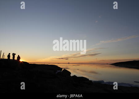 Arancione tramonto sull'acqua con tre persone in ombra con whisp di nuvole Foto Stock