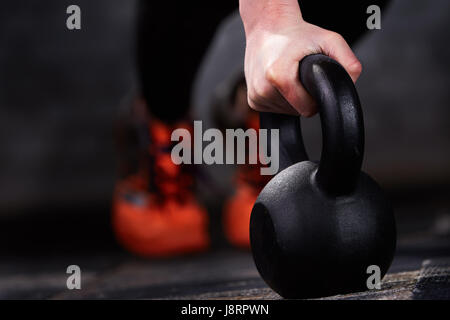 Close-up foto del giovane atleta donna di mano mentre si fa spingere ups su kettlebells contro un muro di mattoni in palestra. Foto Stock