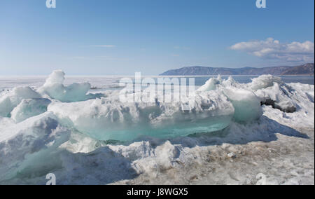 Trasparente blu hummocks ghiaccio sul lago Baikal shore. La Siberia paesaggio invernale vista. Coperto di neve e di ghiaccio sul lago. Grandi crepe nel ghiaccio floe. Foto Stock