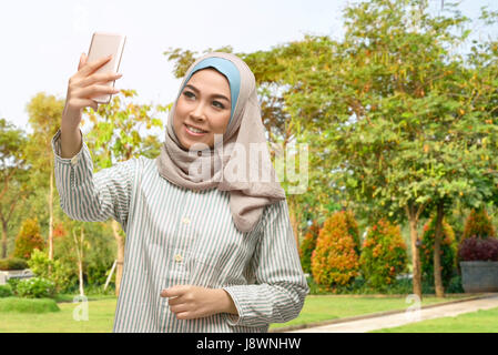 Bella asiatica donna musulmana tenendo selfie foto con lo smartphone sul parco Foto Stock