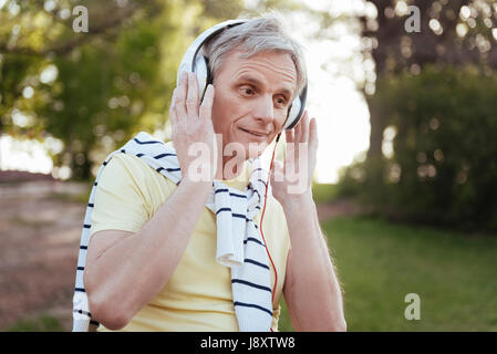 Delizioso uomo senior godendo la musica nelle cuffie all'aperto Foto Stock