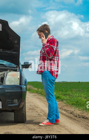 Donna che chiama riparazione auto da strada di campagna, femmina adulta persona in piedi dal veicolo rotto in campagna Foto Stock