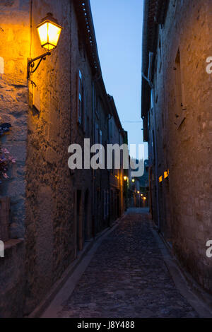 Luce calda da un overhead lampione illumina medievale deserte strade di ciottoli, il 26 maggio, 2017, in Lagrasse, Languedoc-Rousillon, sud della Francia. Lagrasse è elencato come tra i più belli della Francia villaggi e si trova sulla famosa Route 20 Strada del vino nella regione di Basses-Corbieres risalente al XIII secolo. Foto Stock