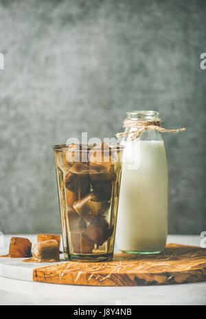 Vetro con caffè congelato di cubetti di ghiaccio e latte in bottiglia Foto Stock