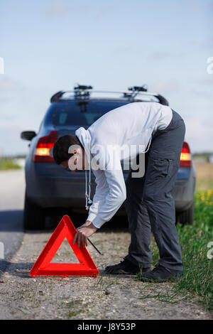 Foto del giovane driver mettendo un triangolo rosso sulla strada vicino a Broken auto nel pomeriggio Foto Stock