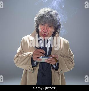 L'uomo anziano come detective o boss della mafia su grigio di sfondo per studio Foto Stock