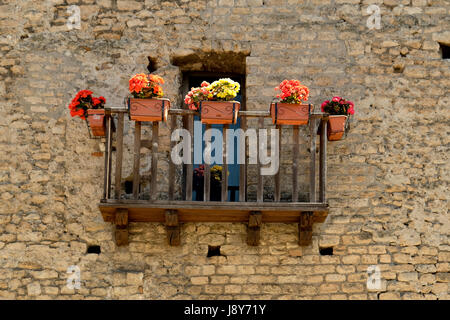 Piccolo balcone in legno con fiori in un'antica facciata fatta con pietre Foto Stock