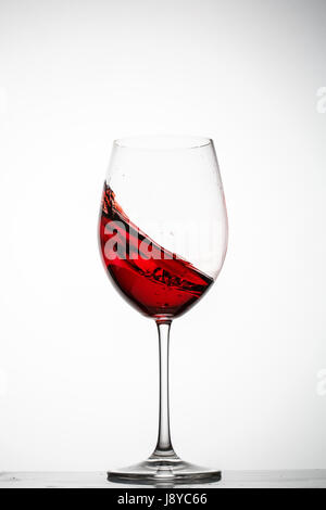 Vino rosso schizzi in un bicchiere su sfondo bianco Foto Stock