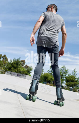 Un giovane uomo caucasico pattinaggio indietro con pattini quad in una all'aperto skate park Foto Stock