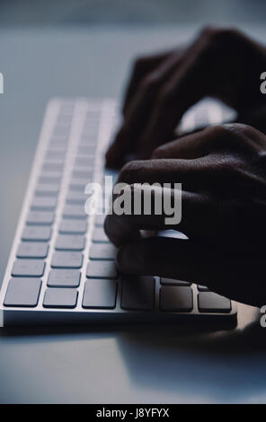 Primo piano di un giovane uomo di digitazione in una tastiera di computer nell'oscurità, con un effetto drammatico Foto Stock