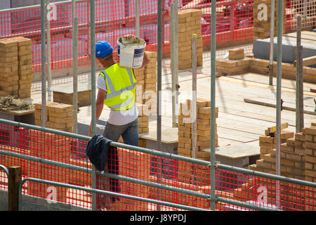 Un sito di costruzione lavoratore o il sistema hod carrier o operaio portando alcuni cemento in una benna Foto Stock