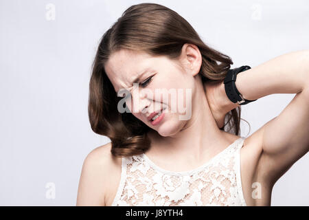 Ritratto di donna bella con le lentiggini e abito bianco e smart guarda con dolore al collo argento su sfondo grigio. Salute e medicina concetto. Foto Stock