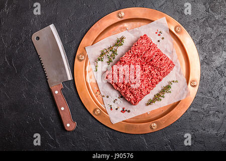 Carni macinate sulla carta e il rame metallico vassoio con il condimento e di timo fresco su sfondo nero, vista dall'alto Foto Stock