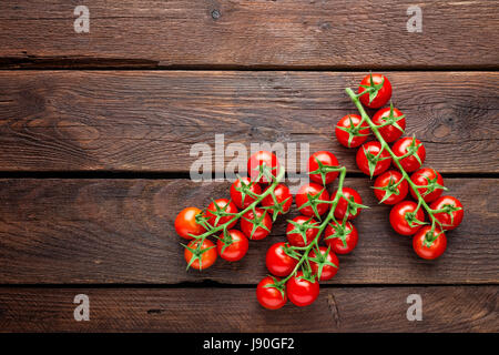 Freschi pomodori ciliegia su ramoscelli sul tavolo di legno, vista dall'alto Foto Stock