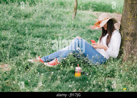Donna rilassante con telefono sotto agli alberi. Guarda come la pellicola fotografica Foto Stock