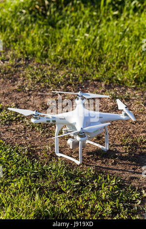 Quadcopter all'aperto, immagini aeree e hobby, concetto di ricreazione - quadrocopter pronti per il decollo, bianco e-osservatore con quattro eliche e fotocamera digitale prima del decollo con estate erba, verticale. Foto Stock