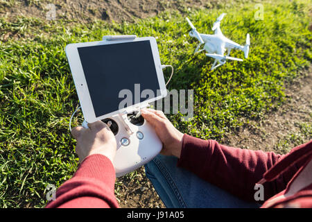 Voli quadcopter all'aperto, immagini aeree e tech hobby concetto - le mani del pilota con telecomando, tablet PC per il sondaggio di volo, la ripresa video e la fotografia aerea, il fuoco selettivo. Foto Stock