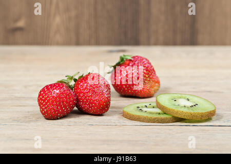 Fragole mature e due fette di kiwi su un vecchio tavolo in legno Foto Stock