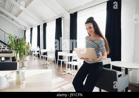 Bella bruna femmina è in piedi e tenendo il suo laptop mentre guardando la telecamera. Foto Stock