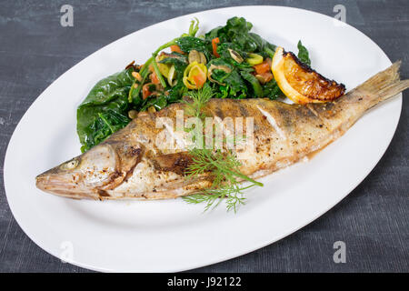 Cotta dorado a caldo con insalata di spinaci. Piastra situata su una tavola nera come sfondo. Foto Stock