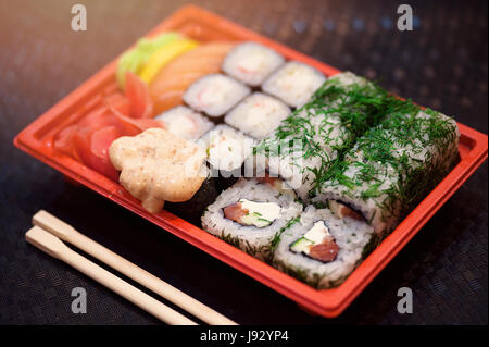 I sushi giapponesi La cucina in plastica rosso Contenitore per il trasporto di alimenti su nero. Rotolo di carne di granchio, avocado, all'interno di cetriolo e masago puzzava roe al di fuori. Foto Stock