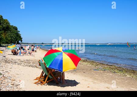 I villeggianti rilassante sulla spiaggia con un colorato ombrellino in primo piano, Studland Bay, Dorset, Inghilterra, Regno Unito, Europa occidentale. Foto Stock