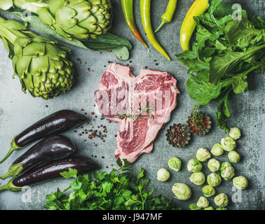 Carne di manzo crudo t-bone steak con spezie e verdure, sullo sfondo di calcestruzzo Foto Stock