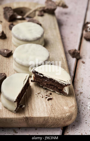 Alcuni argentino uruguayano di alfajores riempito con dulce de leche e rivestito con un rivestimento bianco su un tagliere di legno, su un tavolo rustico Foto Stock