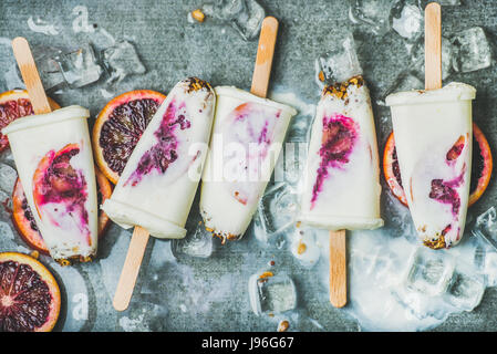 Rosso arancio, yogurt, muesli popsicles su cubetti di ghiaccio, sullo sfondo di calcestruzzo Foto Stock