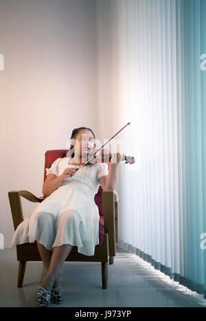 Ragazza asiatica sdraiato sul divano nel soggiorno pratica di suonare il violino con felicità emozione Foto Stock