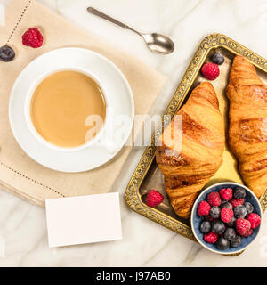 Una foto quadrata di una tazza di caffè con lamponi freschi, mirtilli e croissant, con un fustellato business card con un posto per il testo Foto Stock