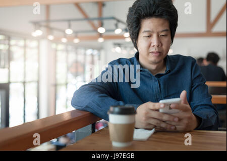 Adulto asiatici imprenditore freelance utilizza lo smartphone per la rete sociale mentre è seduto nella caffetteria sul weekend. Lo stile di vita di relax con caffè Foto Stock