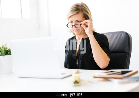 Donna matura in office toccando i suoi occhiali Foto Stock
