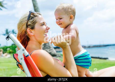 Donna seduta sotto il palm tree con piccolo figlio (18-23 mesi) Foto Stock