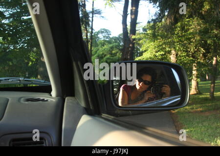 Giovane donna prendendo immagine di se stessa attraverso auto del finestrino laterale Foto Stock