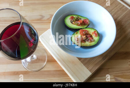 Un avocado e salsa fresca in una ciotola bianca con un bicchiere di vino rosso Foto Stock
