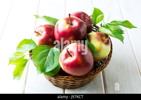 Organici di mele rosse con foglie verdi nel cesto di vimini Foto Stock