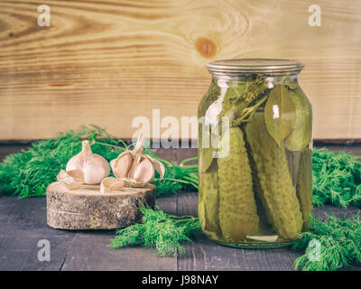 Cetrioli sottaceto su sfondo di legno. Sottaceti in un barattolo di vetro con aglio e aneto fresco. Salate cetriolo in vaso con spazio di copia Foto Stock