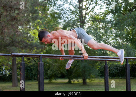 Giovani muscolare di giovane uomo facendo esercizi sulle barre parallele nel parco Foto Stock