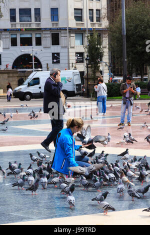 Un turista femminile interrompe l'alimentazione dei branchi di Pigeon in Plaça Catalunya, Barcelona, Catalunya, Spagna Foto Stock