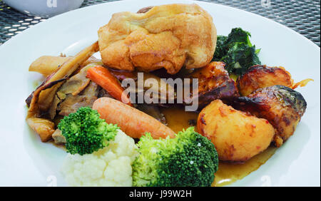 Inglese tradizionale pranzo della domenica il cibo dello Yorkshire pudding, fette di carne, arrosto di patate, carote, broccoli, cavolfiori, spinaci, servita su una bianca Foto Stock